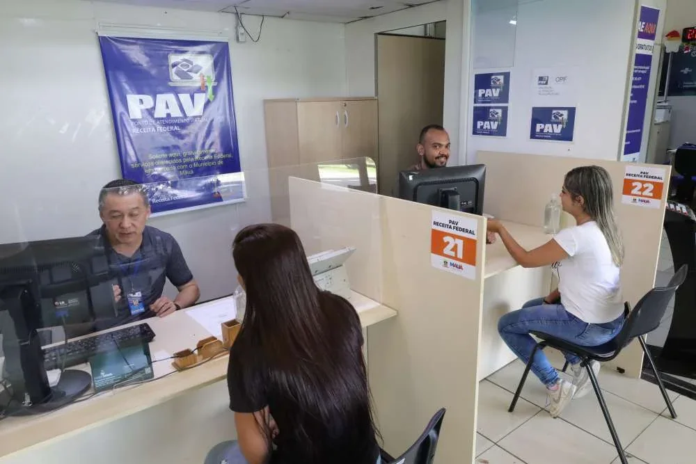 Dois servidores atendem duas mulheres em guichês do Ponto de Atendimento Virtual da Receita Federal, dentro do Paço Municipal de Mauá.
