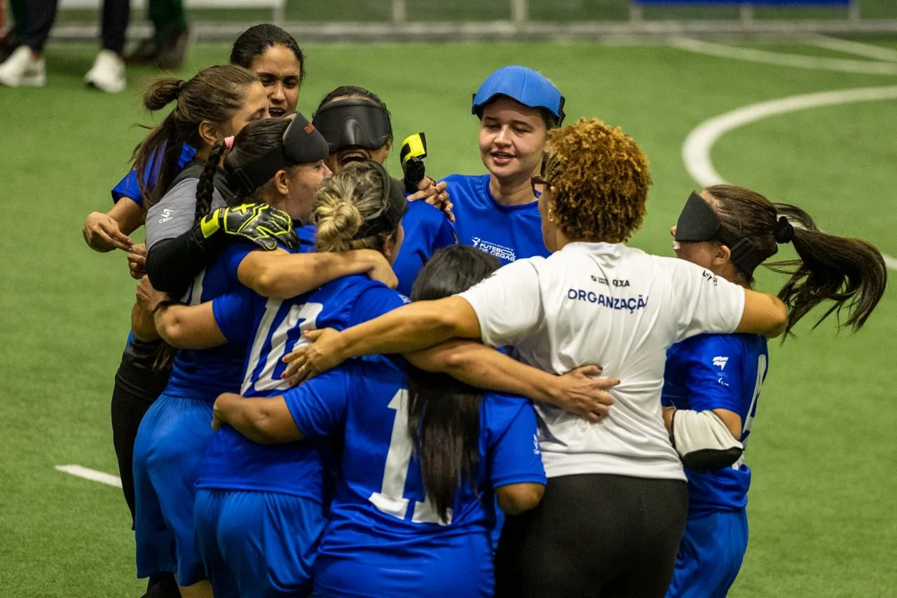 Jogadoras do Centro-Norte, com uniformes azuis e algumas usando vendas, abraçam-se em roda sobre o campo após a conquista do título.