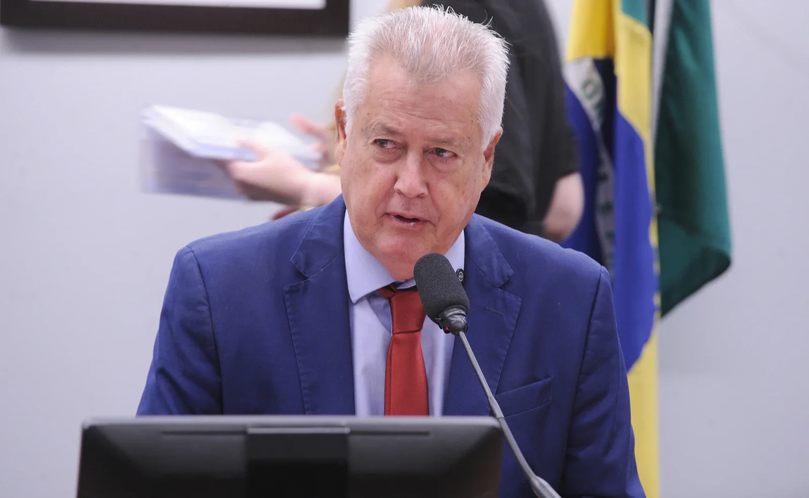 Rodrigo Rollemberg, de terno azul e gravata vermelha, fala ao microfone em uma sala de comissão da Câmara.