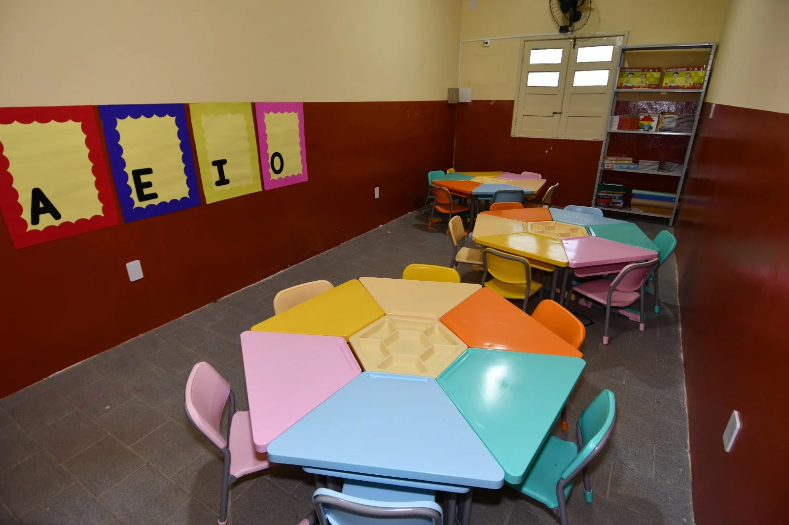 Sala da Escola do Campo de Alagoinhas, com mesas e cadeiras coloridas, cartazes com vogais e estante com livros.