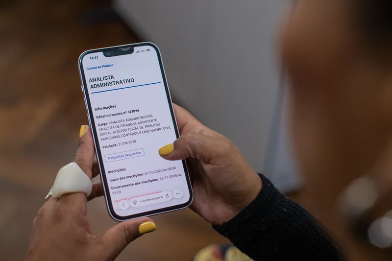 Pessoa segura um celular com informações sobre o cargo de analista administrativo no concurso da Prefeitura de Curitiba.