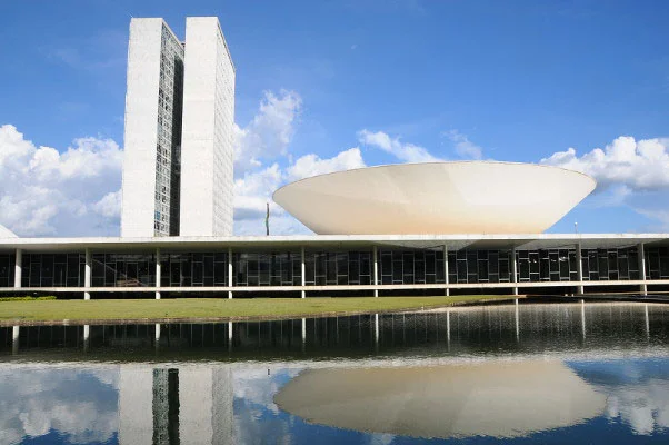 Fachada do Congresso Nacional, com torres e cúpulas refletidas no espelho d’água.