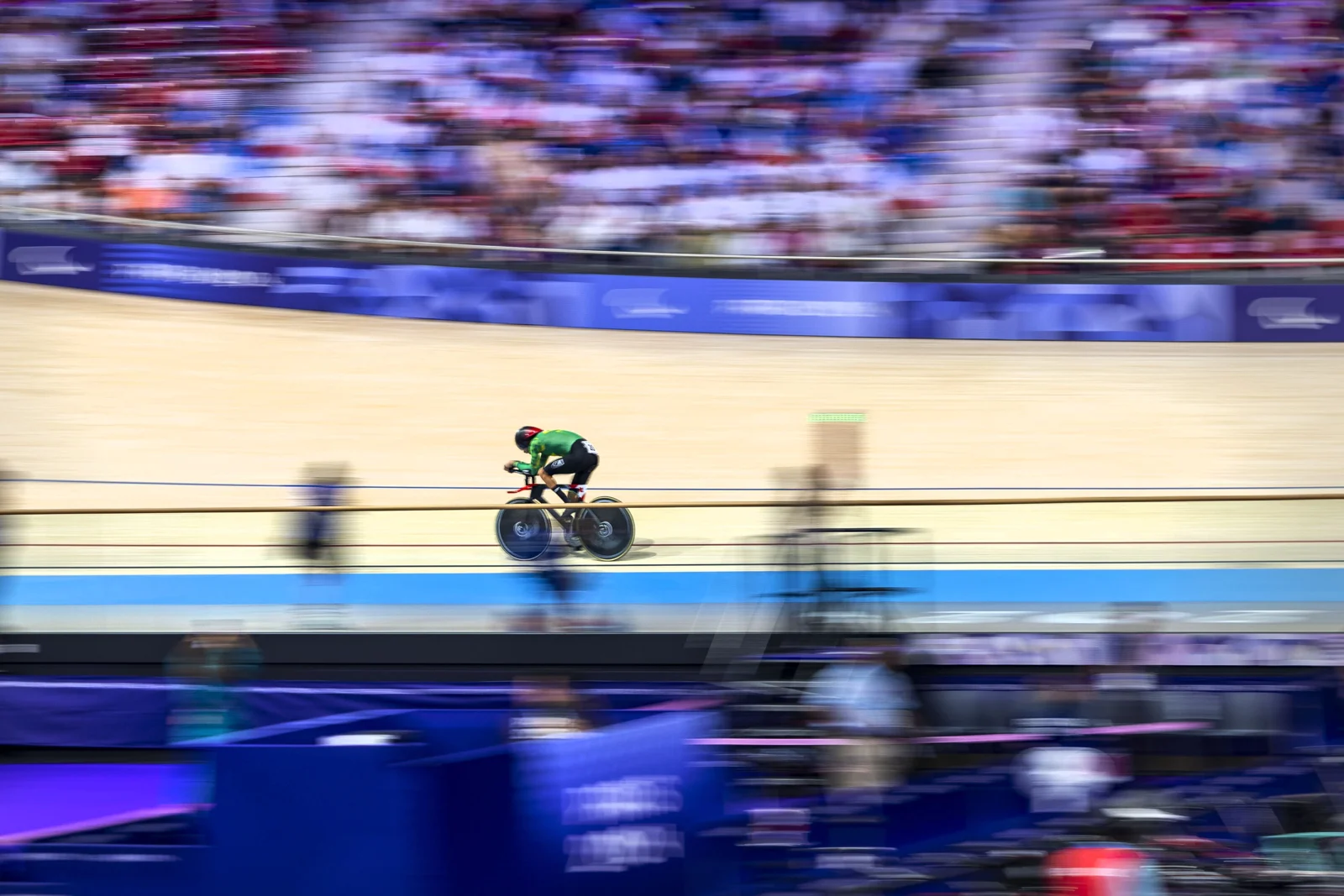 Lauro Chaman, com uniforme verde, pedala em um velódromo diante de arquibancadas desfocadas pelo movimento.