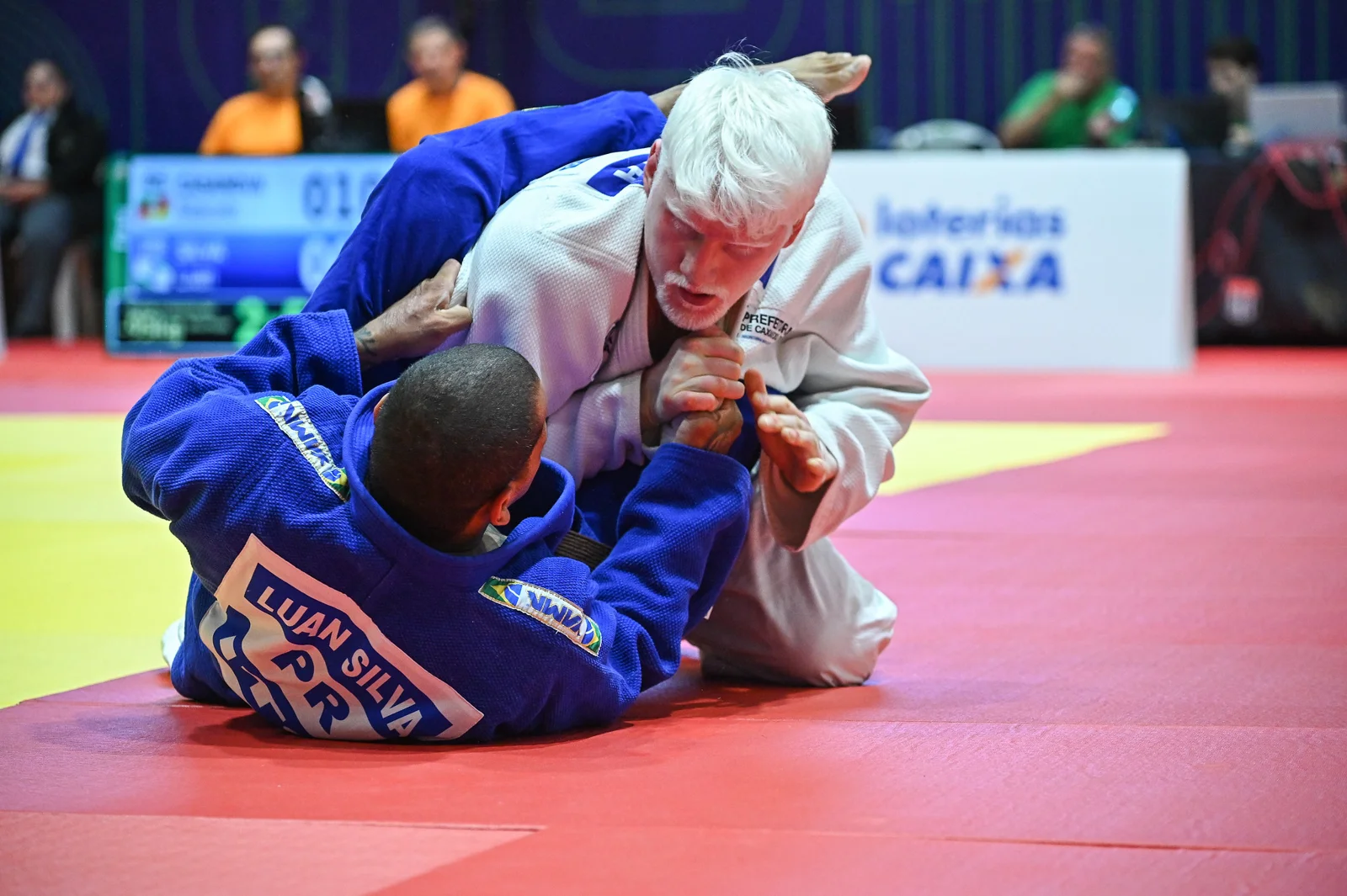 Marcelo Casanova, de quimono branco, disputa um lance no solo com um adversário de quimono azul.