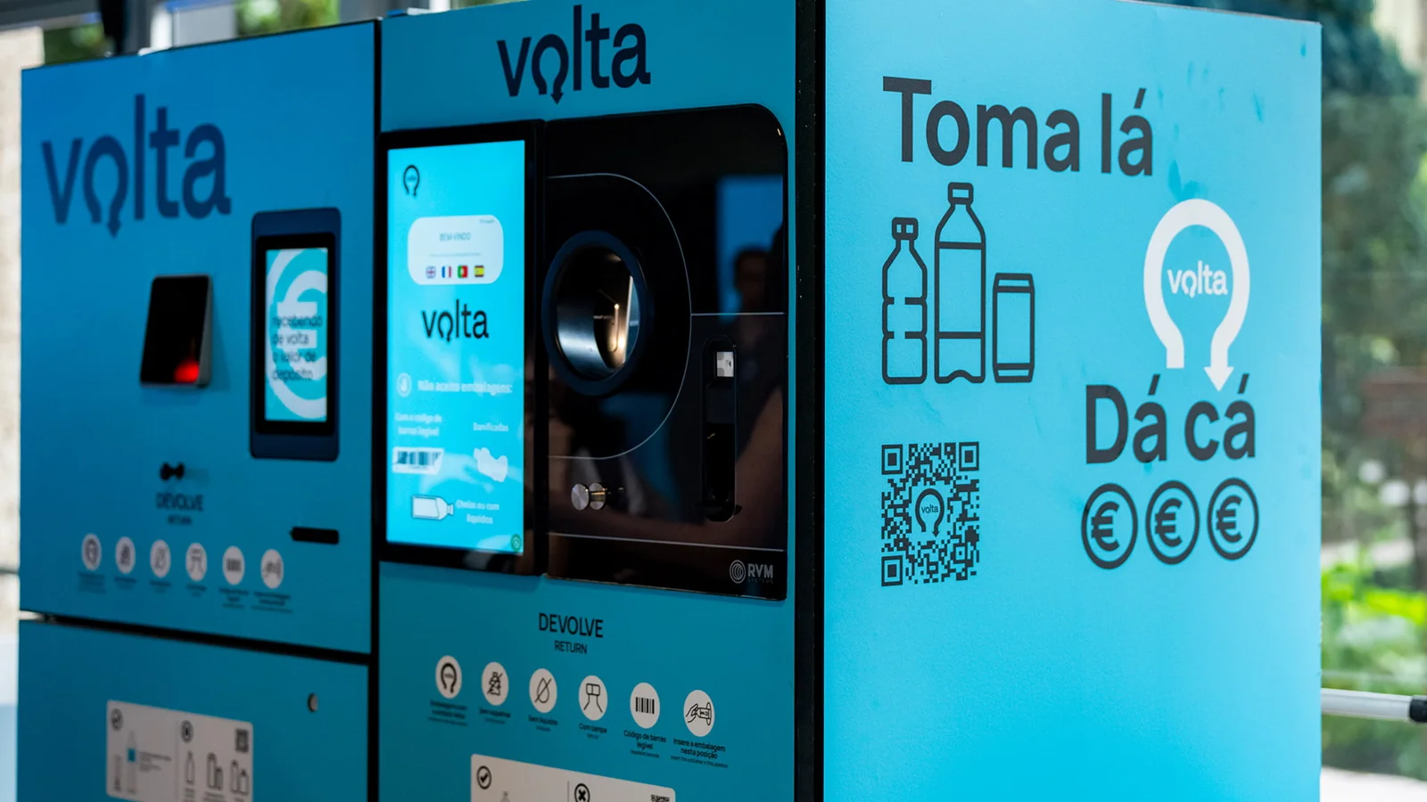 Máquina azul do sistema Volta, com tela, abertura para receber embalagens e instruções impressas na lateral.