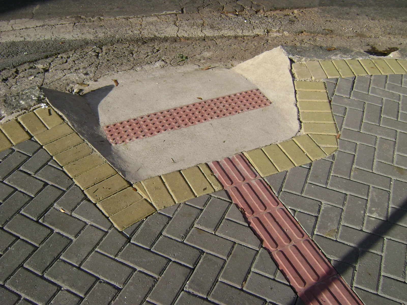 Piso tátil direcional rosa conduz a uma rampa de calçada, com faixa de alerta junto à rua, em Belo Horizonte.