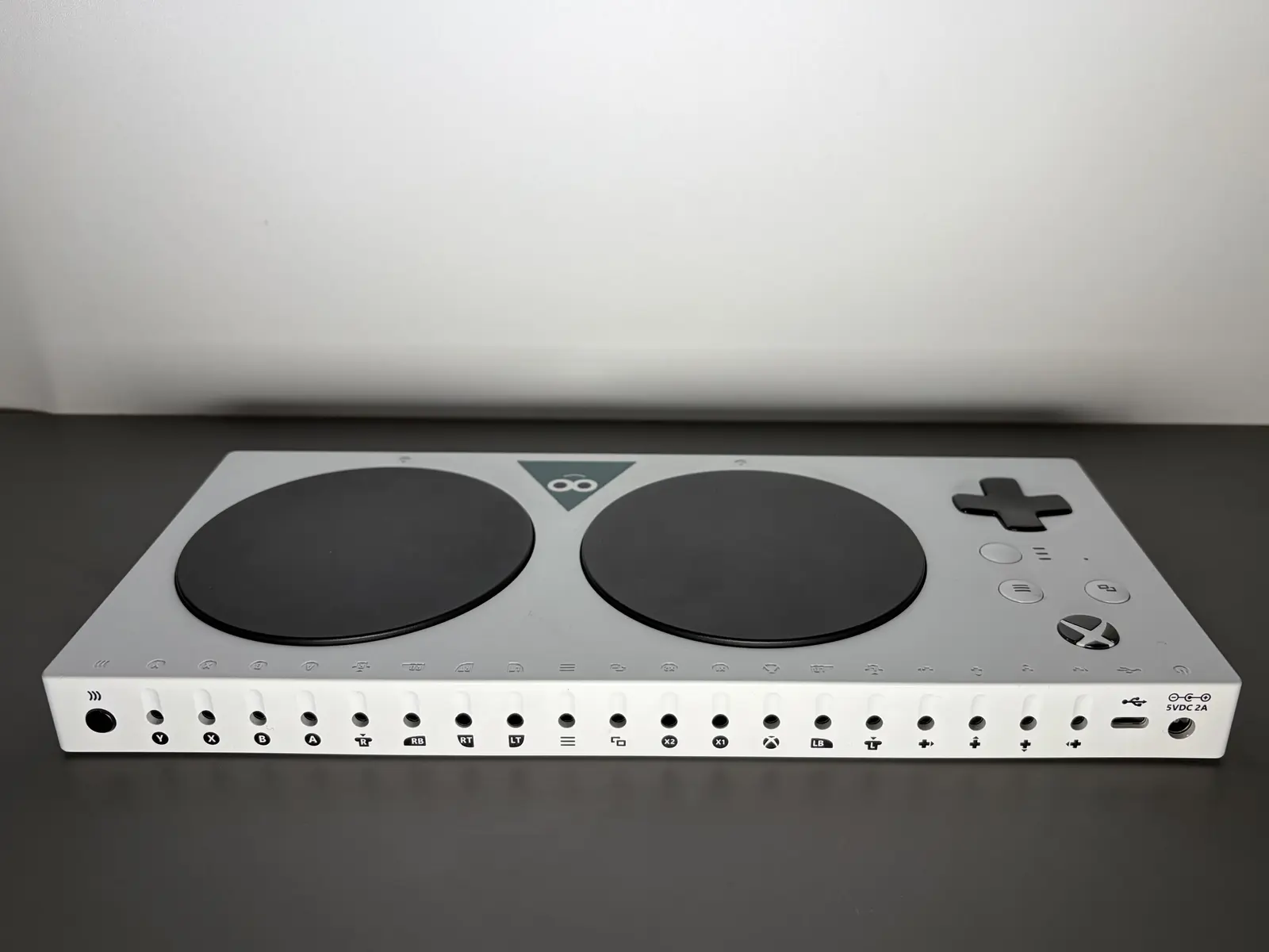 Controle adaptativo Xbox branco sobre uma mesa cinza, com dois grandes botões pretos, direcional e entradas para conectar acessórios.