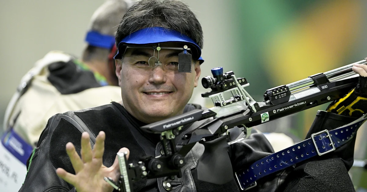 Marcelo Marton sorri usando viseira azul e óculos de tiro, enquanto segura uma carabina durante competição no Rio de Janeiro. Foto de arquivo.