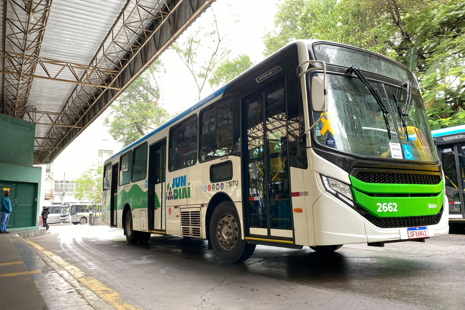 Ônibus branco e verde do transporte coletivo de Jundiaí está parado em um terminal coberto.
