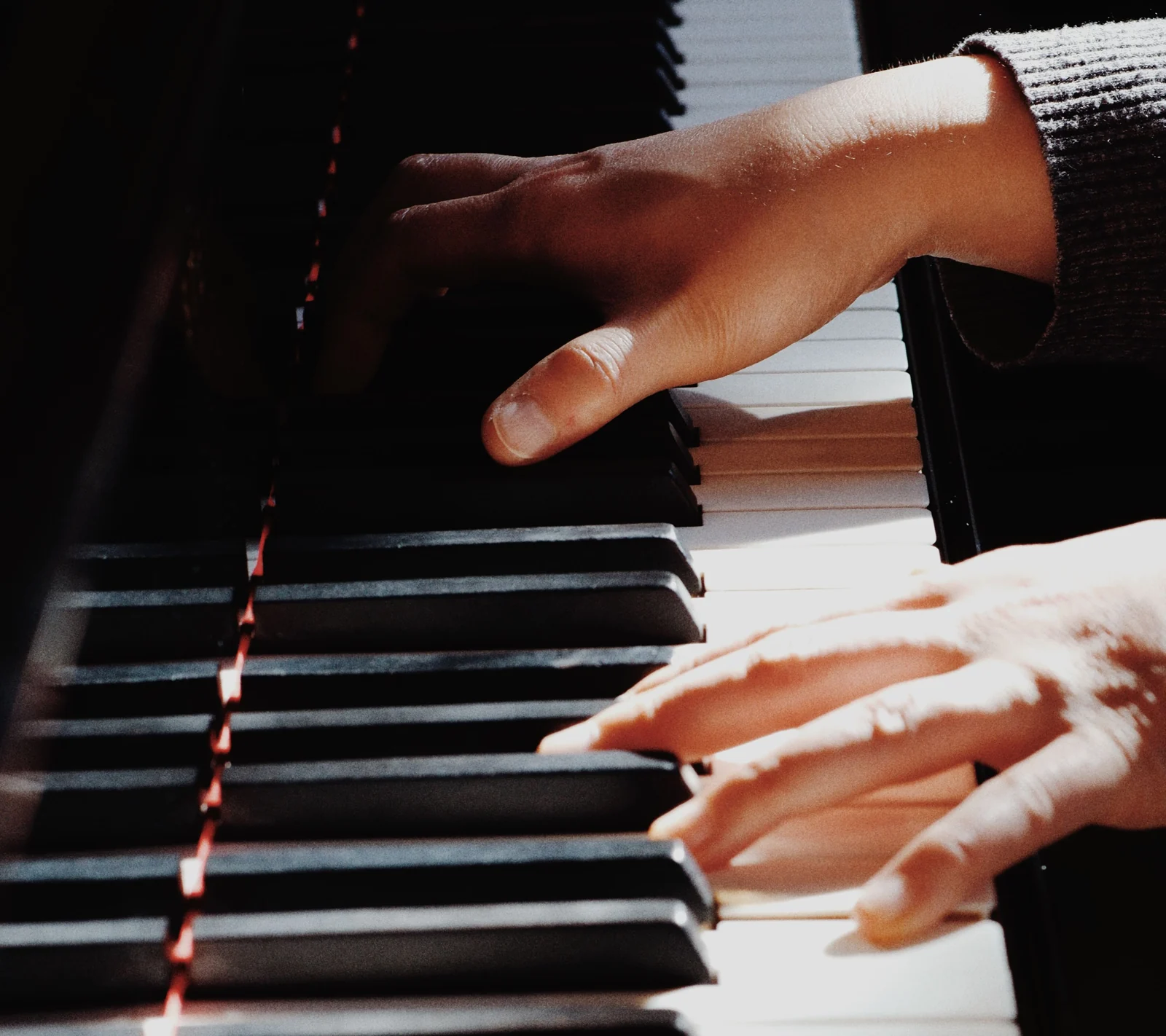 Duas mãos sobre as teclas brancas e pretas de um piano.