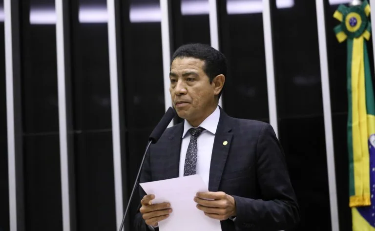 Deputado Pastor Gil, de terno escuro, segura folhas de papel e fala ao microfone na Câmara dos Deputados.