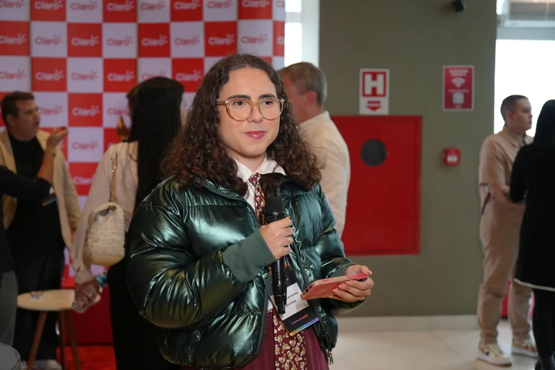 Eduardo Victor, de óculos e jaqueta verde, segura um microfone e um celular durante a edição de 2025 do Link Festival.