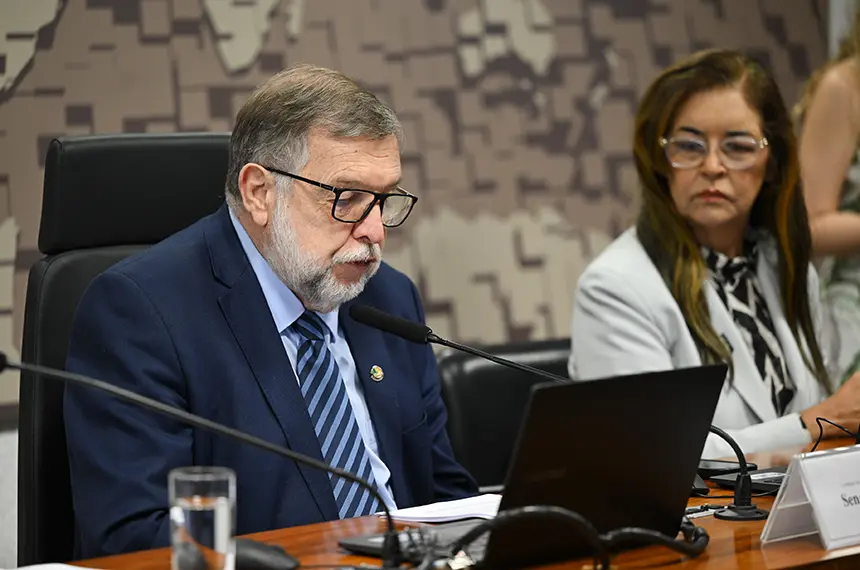 O senador Flávio Arns, de óculos, terno azul e gravata listrada, fala ao microfone diante de um notebook; ao lado, a senadora Dra. Eudócia acompanha a reunião.