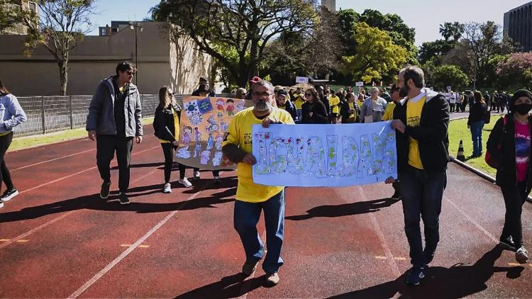 Participantes caminham por uma pista de atletismo carregando cartazes coloridos durante os jogos de estudantes em Porto Alegre, em foto de arquivo de 2022.