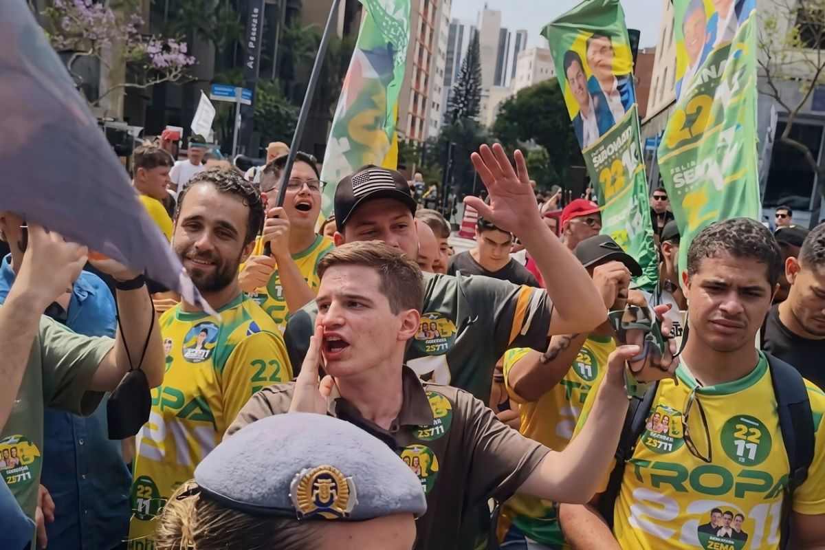 Lucas Pavanato grita com uma das mãos próxima à boca, cercado por apoiadores vestidos de amarelo e verde na Avenida Paulista.